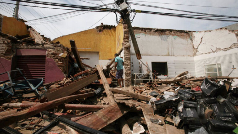 Vivienda de una planta derrumbada por el terremoto, con la fachada caída sobre la acera y escombros cubriendo la calzada