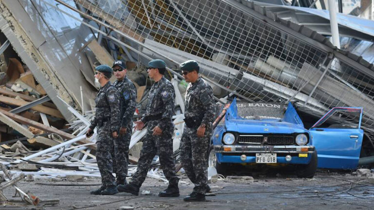 Policías junto a un vehículo aplastado por la estructura metálica de un edificio colapsado