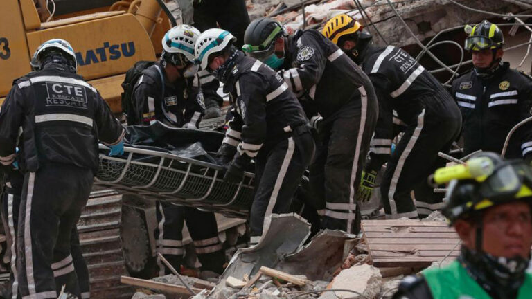 Personal de la CTE, bomberos y socorristas trasladan una camilla sobre los escombros de una edificación colapsada