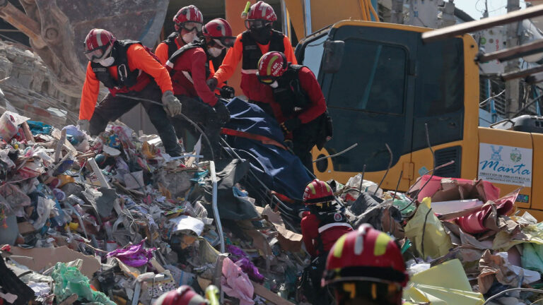Cuadrilla de rescate y una excavadora trabajan sobre un montículo de escombros y enseres domésticos