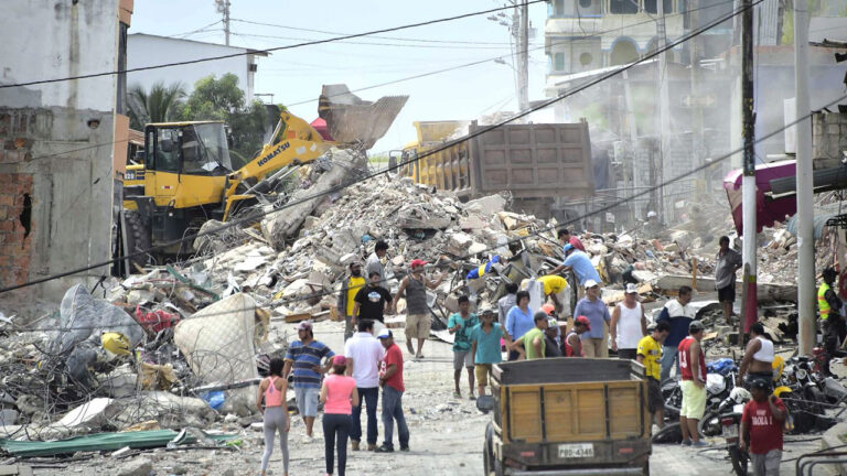 Maquinaria pesada carga escombros en volquetes mientras los vecinos observan la remoción en una calle afectada