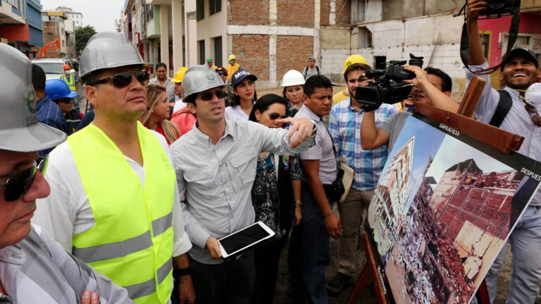 Autoridades y técnicos con casco revisan en terreno una lámina con el registro fotográfico de una edificación afectada