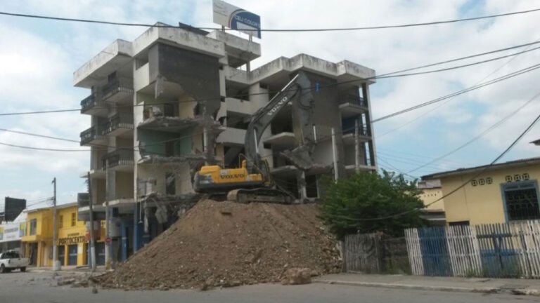 Excavadora demoliendo un edificio de varios pisos con daño estructural en una calle de Manabí