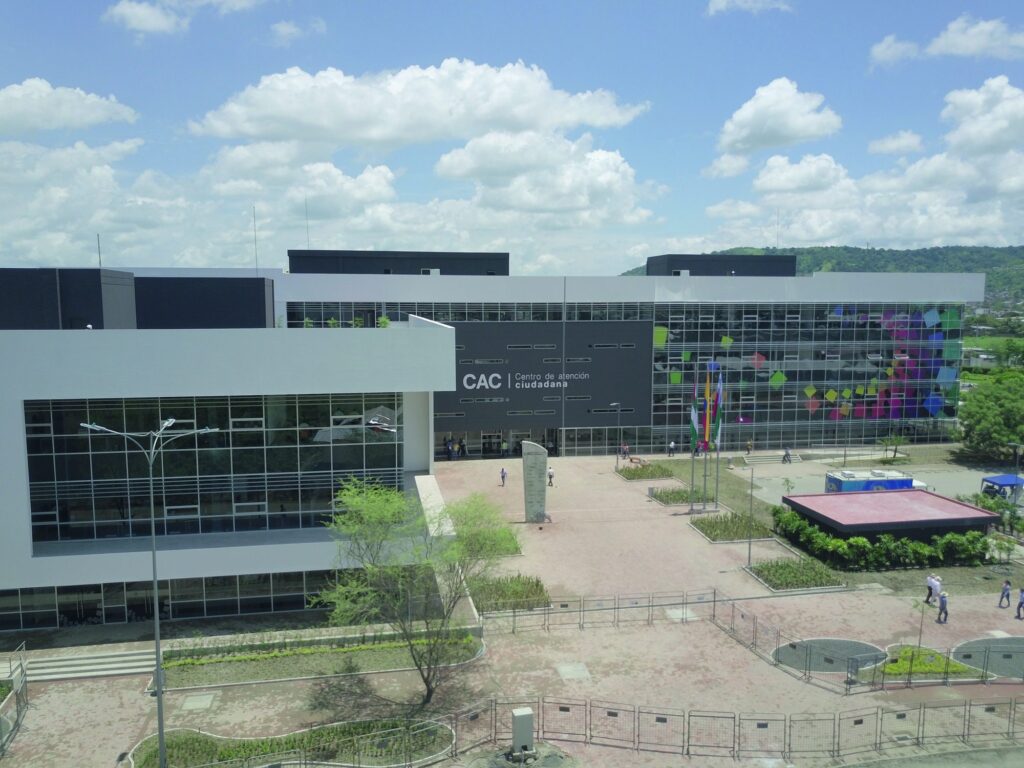 Fachada principal del Centro de Atención Ciudadana de Portoviejo con banderas izadas y ciudadanos cruzando la explanada