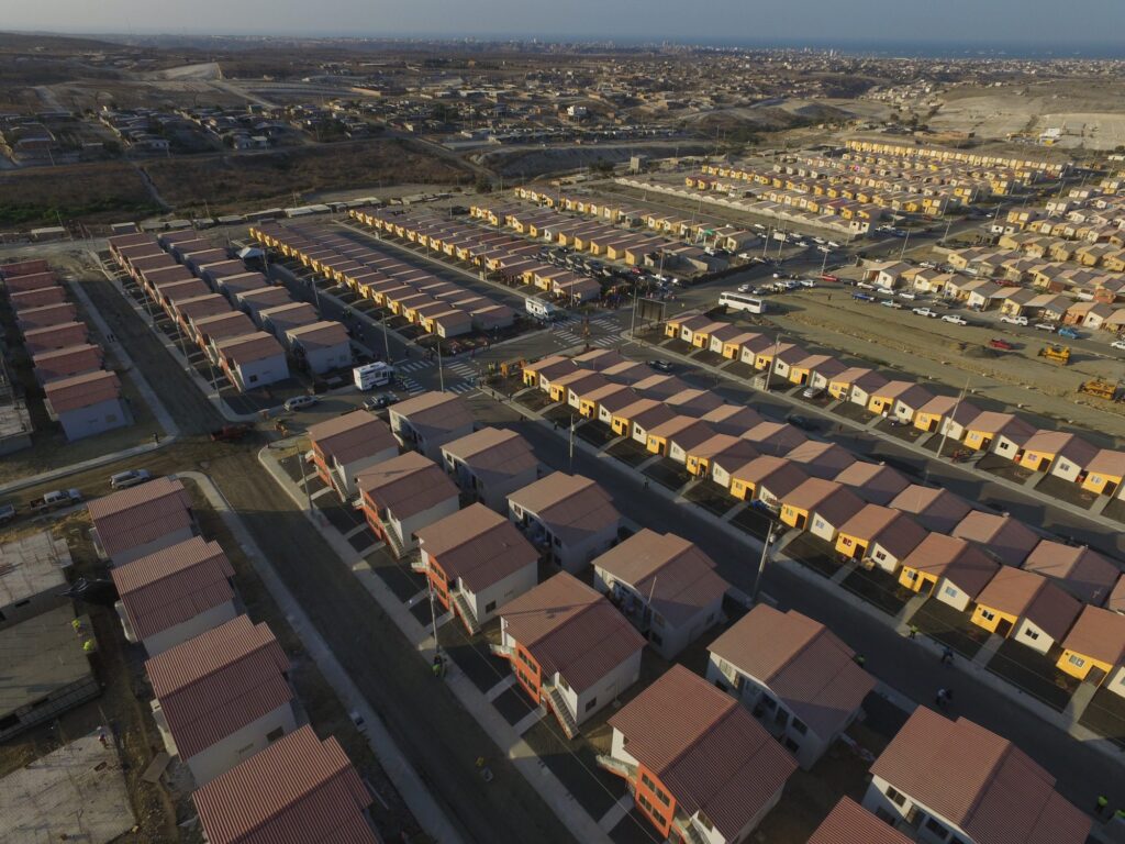 Vista aérea de la ciudadela Si Mi Casa en Manta, con cientos de viviendas alineadas y la ciudad al fondo