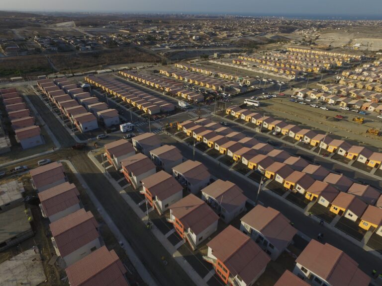 Vista aérea de la ciudadela Si Mi Casa en Manta, con cientos de viviendas alineadas y la ciudad al fondo