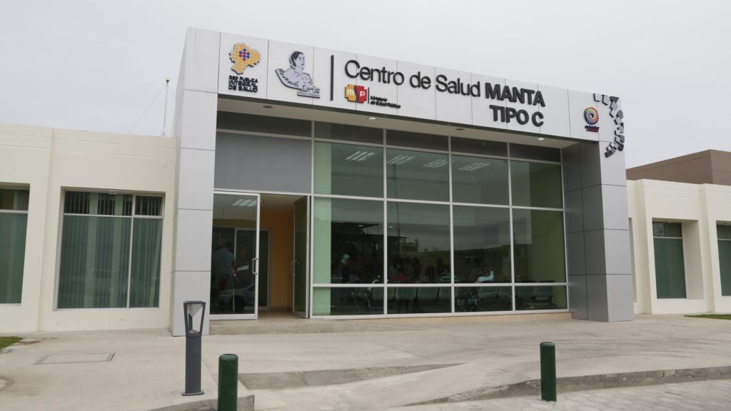 Fachada del Centro de Salud Manta Tipo C terminado, con ingreso acristalado y sala de espera ocupada por pacientes