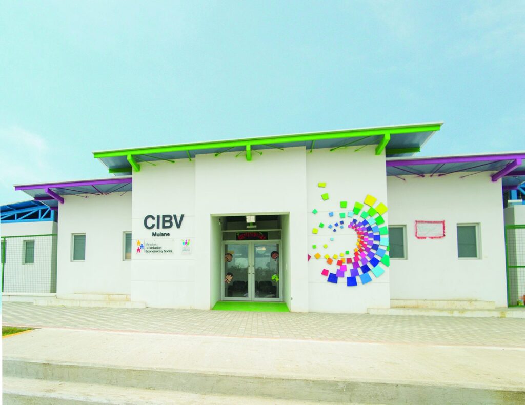 Fachada del Centro Infantil del Buen Vivir de Muisne, con mural de colores, aleros verdes y morados, y cartel de bienvenida