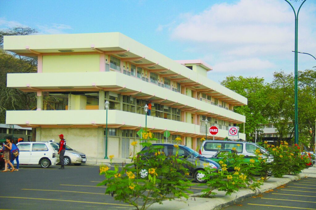 Edificio de la Universidad Técnica de Manabí en proceso de reparación, con obreros trabajando en la fachada de tres plantas