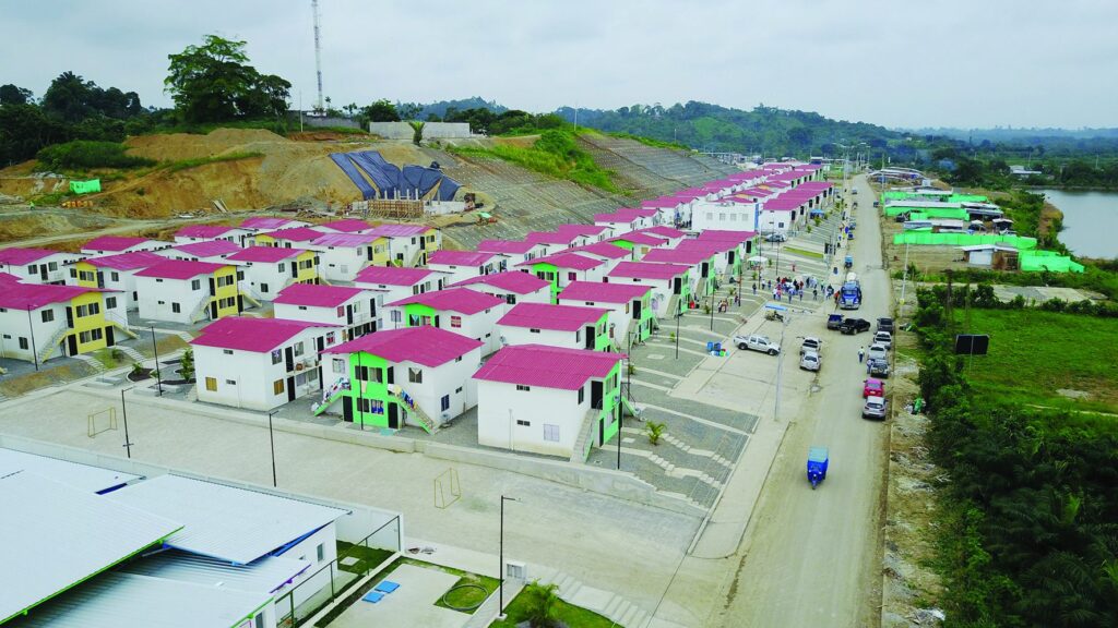 Vista aérea del conjunto habitacional de Nuevo Muisne, con viviendas de techo rojo, vía de acceso y habitantes en la calle