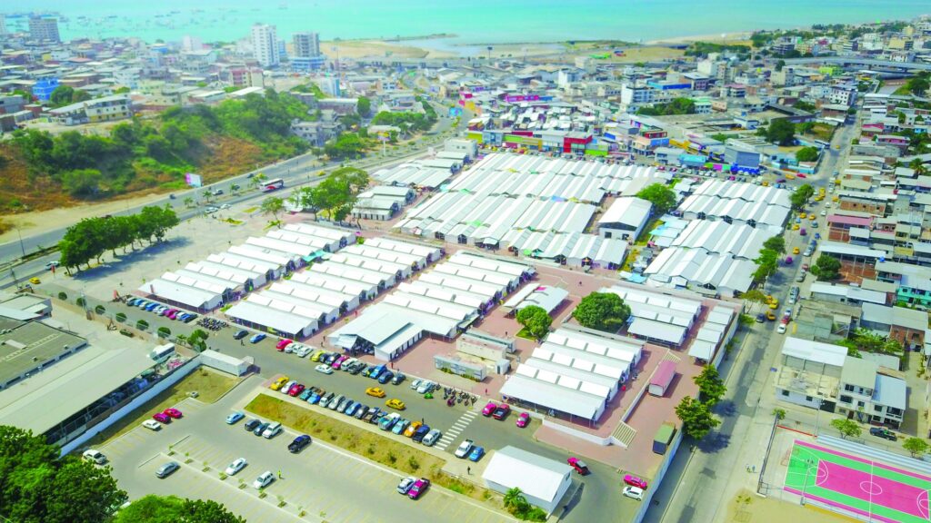Vista aérea de la zona comercial de Nuevo Tarqui en Manta, con decenas de locales de techo blanco ocupados por comerciantes y el mar al fondo