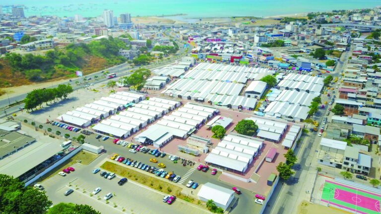 Vista aérea de la zona comercial de Nuevo Tarqui en Manta, con decenas de locales de techo blanco ocupados por comerciantes y el mar al fondo